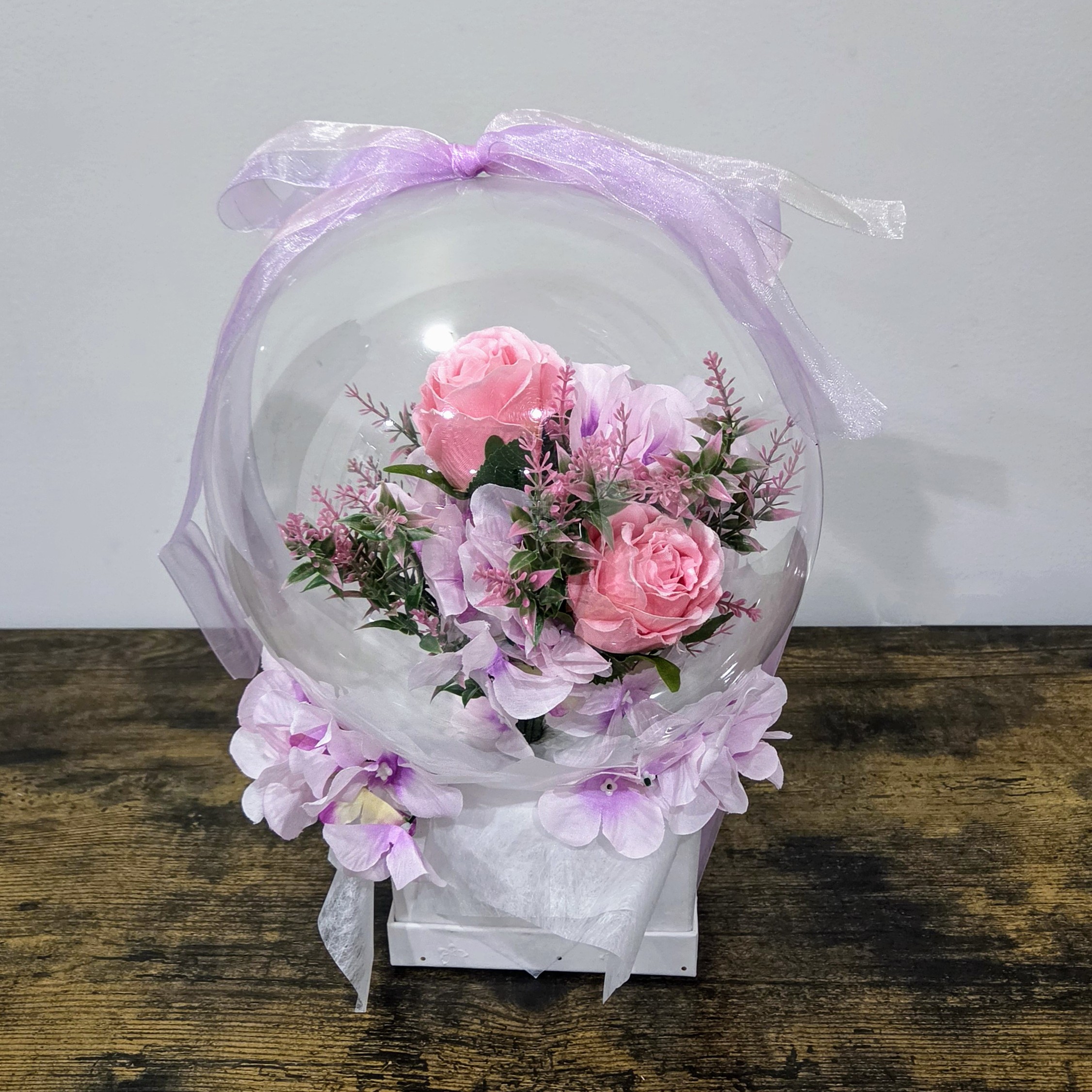Pink roses in transparent bobo balloon with purple ribbon gift